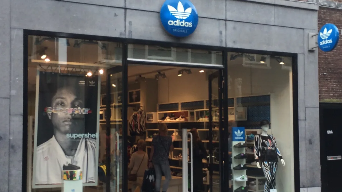 Витрина и вход магазина Adidas Originals: фирменная вывеска над стеклянной дверью, внутри видны полки с кроссовками